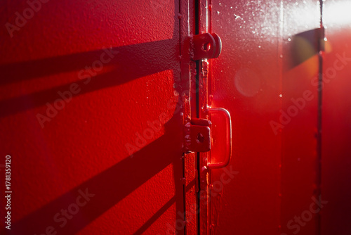 Fotografie Close-up of red-painted metal door with welded handle, brackets, and visible sun