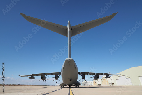 Tactical transport aircraft seen from behind showing tail structure and engines under clear sky
