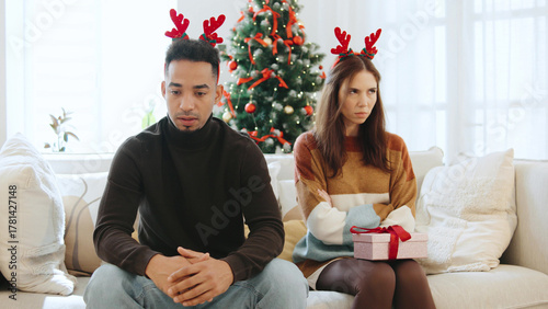 Multiracial couple offended by each other during Christmas time feeling disconnected while sitting by the decorated Christmas tree at home