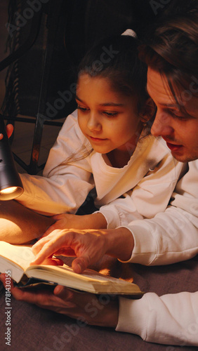 Daughter and father reading together with a flashlight during co