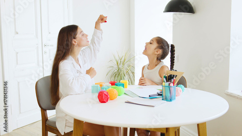 A speech therapist interacts with a child during a therapy session, utilizing colorful toys to enhance communication skills in a well-lit, contemporary setting.