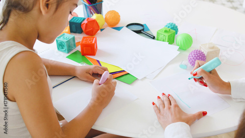 Child engages in creative drawing alphabet with a speech therapist in a bright therapy room focusing on communication skills development