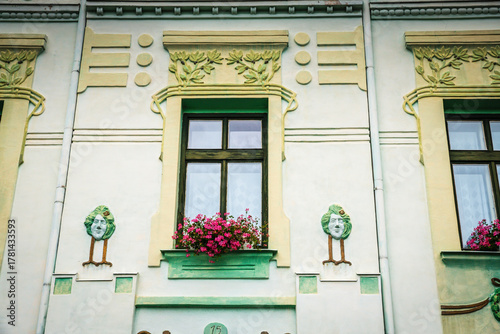 Colorful fresco of faces and flowers, and a pink floral windowbox, on a historic building in Kutná Hora, Czech Republic.