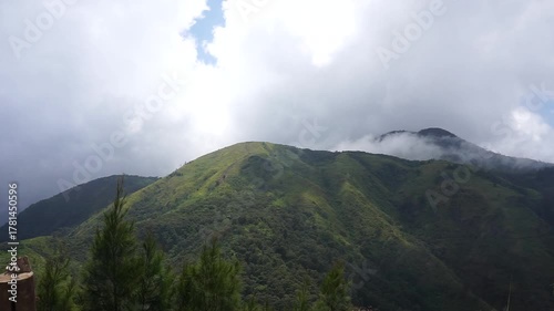 A scenic view of lush green mountains under a cloudy sky, with hints of sunlight.