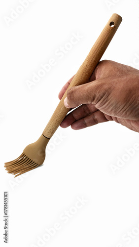 Foto hand holding a brown silicone basting brush with wooden handle isolated on white