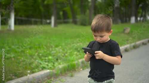 Little boy walking in park looking at smartphone screen 4k