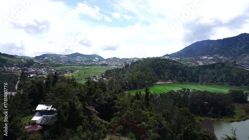 Scenic overview of a lush green landscape with mountains, trees, and a distant town under a cloudy sky.