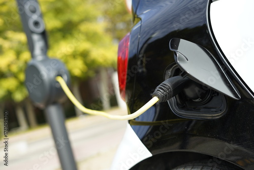 Detalle de un coche eléctrico con el puerto de carga y enchufe conectado con cable para la carga de batería en la calle en una estación de carga