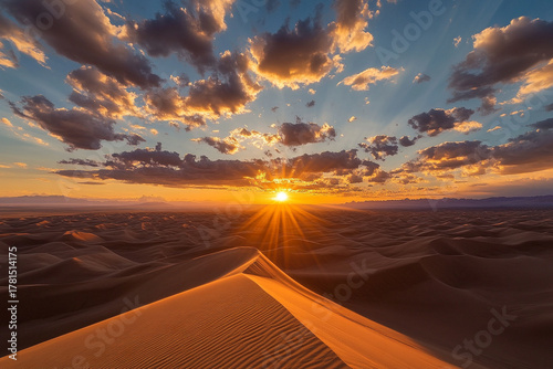 Fototapeta Naklejka Na Ścianę i Meble -  breathtaking sunset over rolling sand dunes, where scattered clouds glow in rich amber tones
