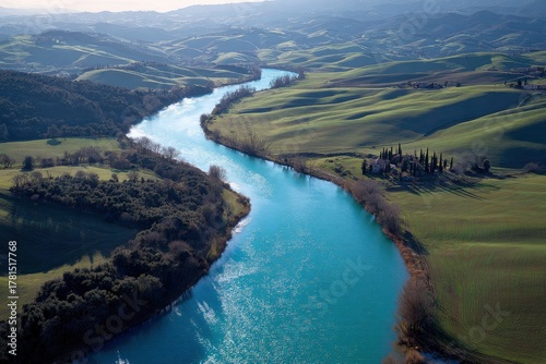 Aerial view showcases a winding river flowing through rolling green hills under soft, diffused