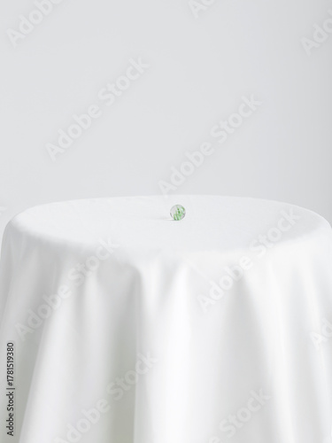A glass ball sits on a white tablecloth against a white background.