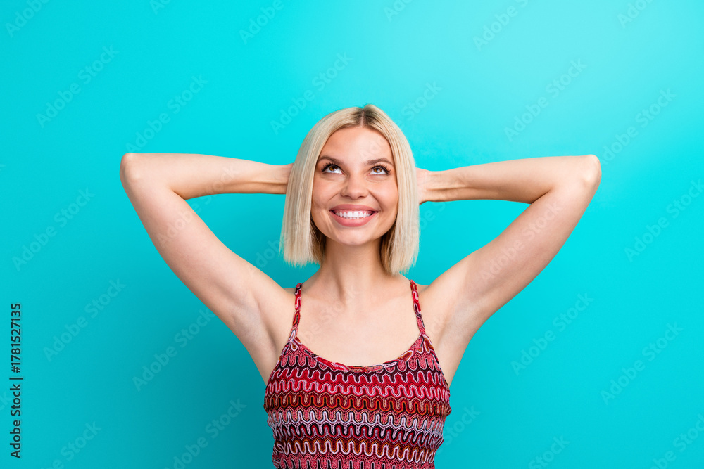 Fototapeta premium Young woman with blonde bob smiles with hands behind head wearing a patterned tank top against teal background showcasing lifestyle fashion and positive energy