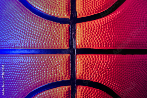 Detailed basketball, showcasing its textured surface and black seams under vibrant neon lighting