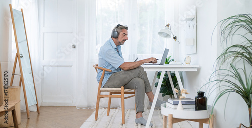 Portrait of happy caucasian business senior man casual cloths shirt work in home office desk using head phone computer. Small business employee freelance online sme marketing e-commerce telemarket