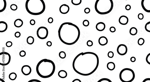A playful, seamless pattern featuring an array of hand-drawn black circles and rings of various sizes on a crisp white background.