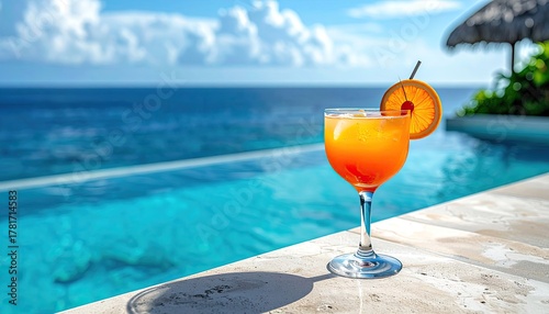 Fototapeta Naklejka Na Ścianę i Meble -  Tropical Orange Cocktail Refreshment by Infinity Pool Overlooking Deep Blue Ocean on Sunny Day with Palm Trees and White Sand Beach Visible in Background