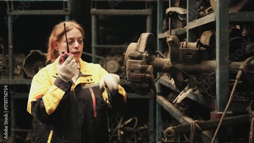 One Hispanic mature female inspector remotely works with walkie-talkie, checks auto spare parts stock in warehouse stack, operates jobs in manufacturing factory, and industrial worker occupation.