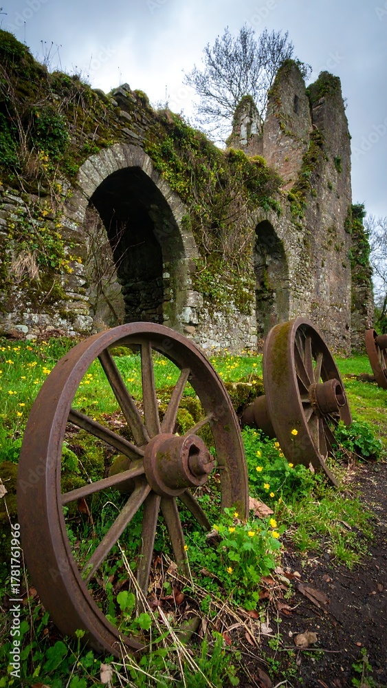 Obraz premium Rusty wagon wheels sit by ancient castle ruins