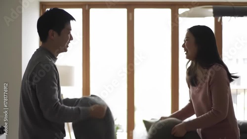 Young couple having fun pillow fight in home living room near window, using for relationship concept