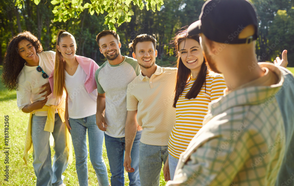 Naklejka premium Company of happy young friends talking with each other standing in summer park. Smiling men and women students in casual clothes communicating gathering in nature outdoors. Friendship concept.