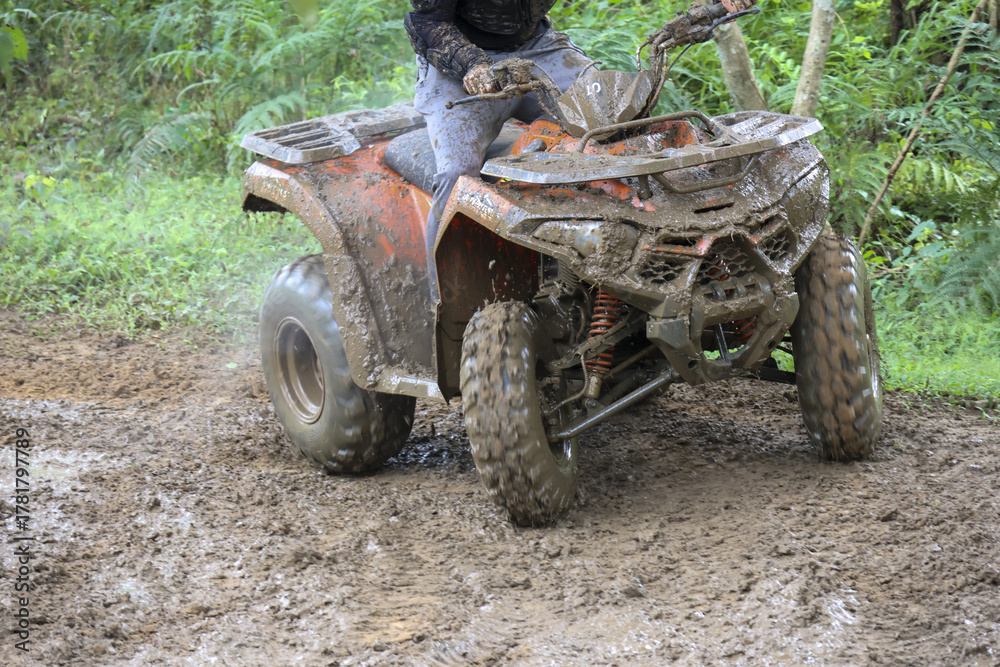 Fototapeta premium Thrilling off road adventure with person riding quad bike through muddy terrain. An exciting motorsport activity in forest on dirty four wheeler vehicle for fun