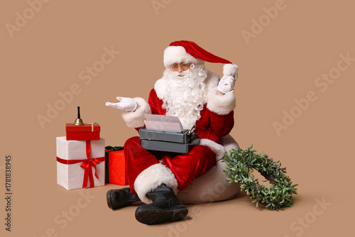 Santa Claus with vintage typewriter sitting on beanbag chair against brown ba...