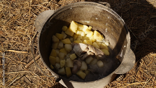 Rustic stew cooking in a pot outdoors. Campfire meal with potatoes and meat. Traditional outdoor cooking in cast iron pot. Boiled potatoes and meat in metal pot.
