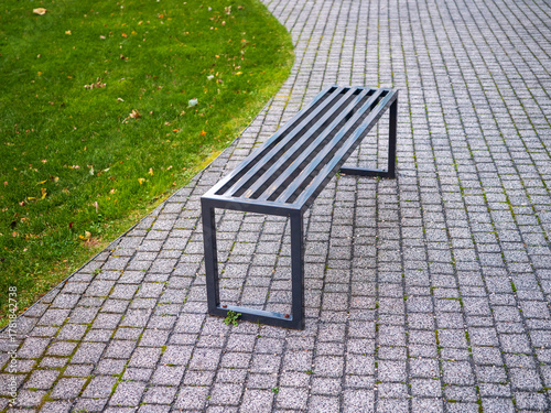 Wallpaper Mural Modern metal park bench on stone pavement with green grass, ideal for rest and walks in an urban park. Torontodigital.ca