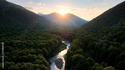 Aerial drone shot of lush green mountains at sunrise, revealing a winding river through a dense forest outdoor, revealing, background