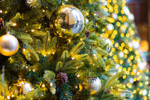 Christmas decoration golden ball closeup tree. A detailed view of warm, glowing Christmas tree branches adorned with reflective gold ornaments, small lights, and pine cones