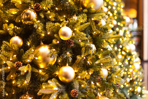 Christmas decoration golden ball closeup tree. A detailed view of warm, glowing Christmas tree branches adorned with reflective gold ornaments, small lights, and pine cones