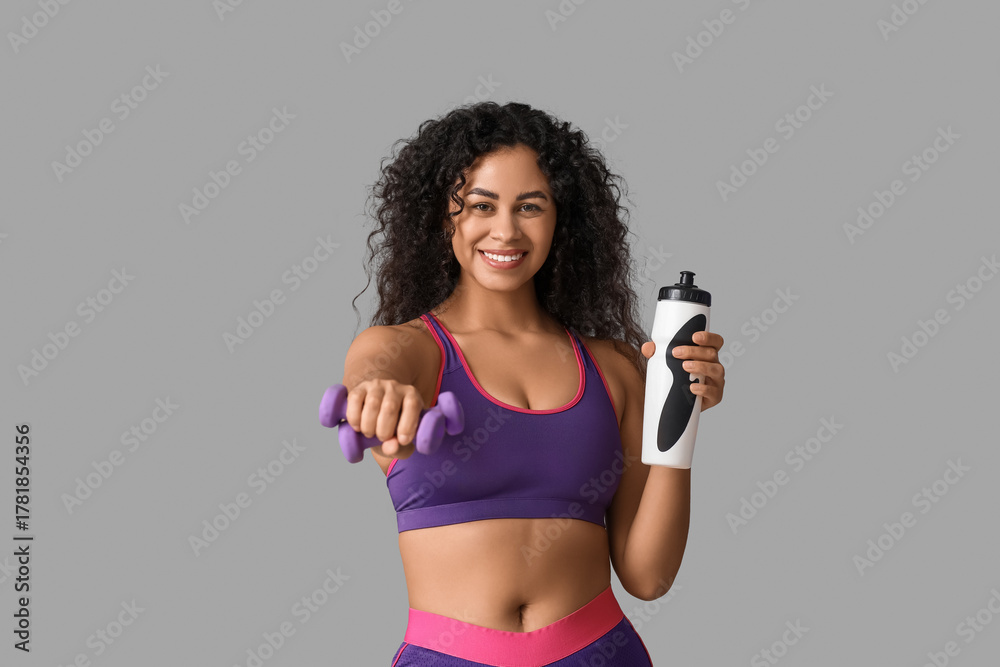 Naklejka premium Sporty young African-American female coach with water bottle and dumbbells on white background