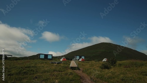View of campsite with tents and guest houses in valley at foot of green hills for relaxation among beauty of wild nature. Concept of silence and pacification