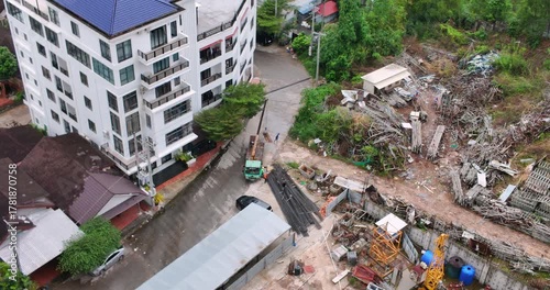 
At a construction site next to an apartment building, workers use a crane truck to move a bin near a pile of steel beams.