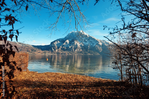 Scenic view of tranquil lake surrounded by autumn foliage and majestic mountain peaks under a clear blue sky, showcasing natural beauty and serenity