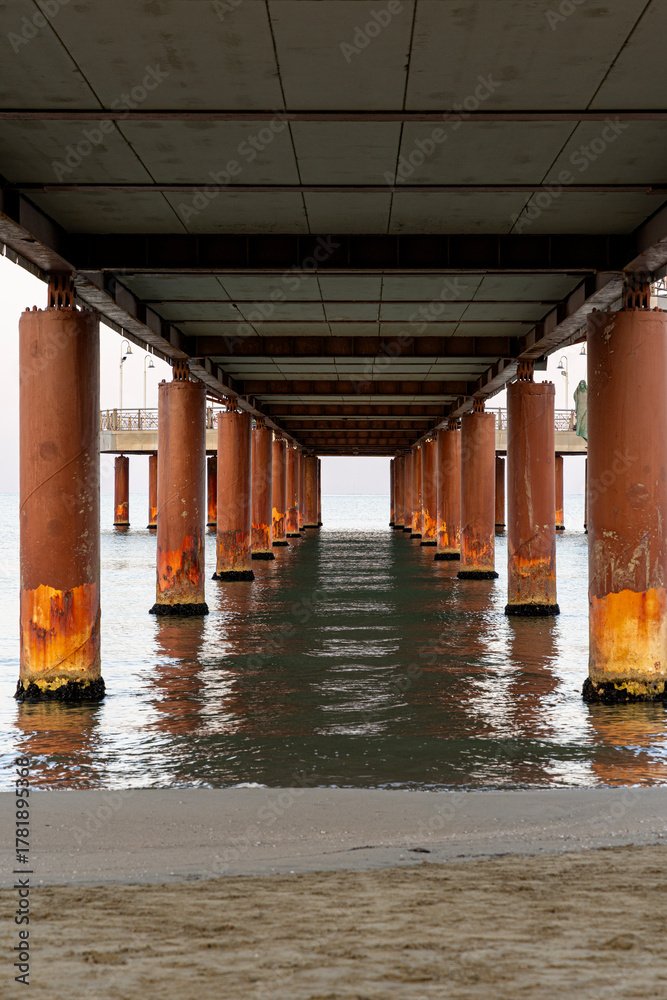 Fototapeta premium Pedestrian pier extending far out to sea, washed by the waves. View from under the bridge. Viareggio, Italy.
