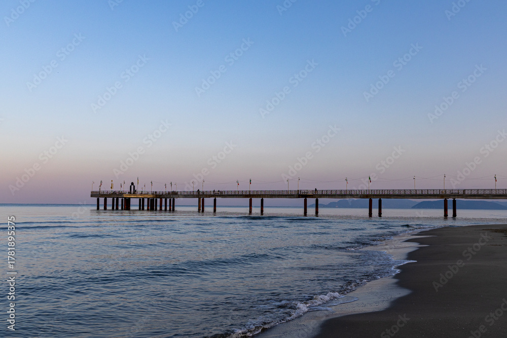 Fototapeta premium Pedestrian pier extending far out to sea, washed by the waves. Viareggio, Italy.