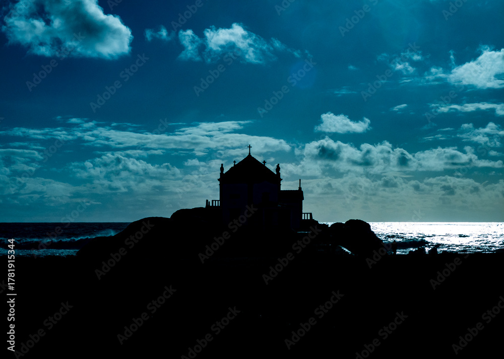 Obraz premium Silhouette of a church on a rocky outcrop with the ocean and sky in the background.