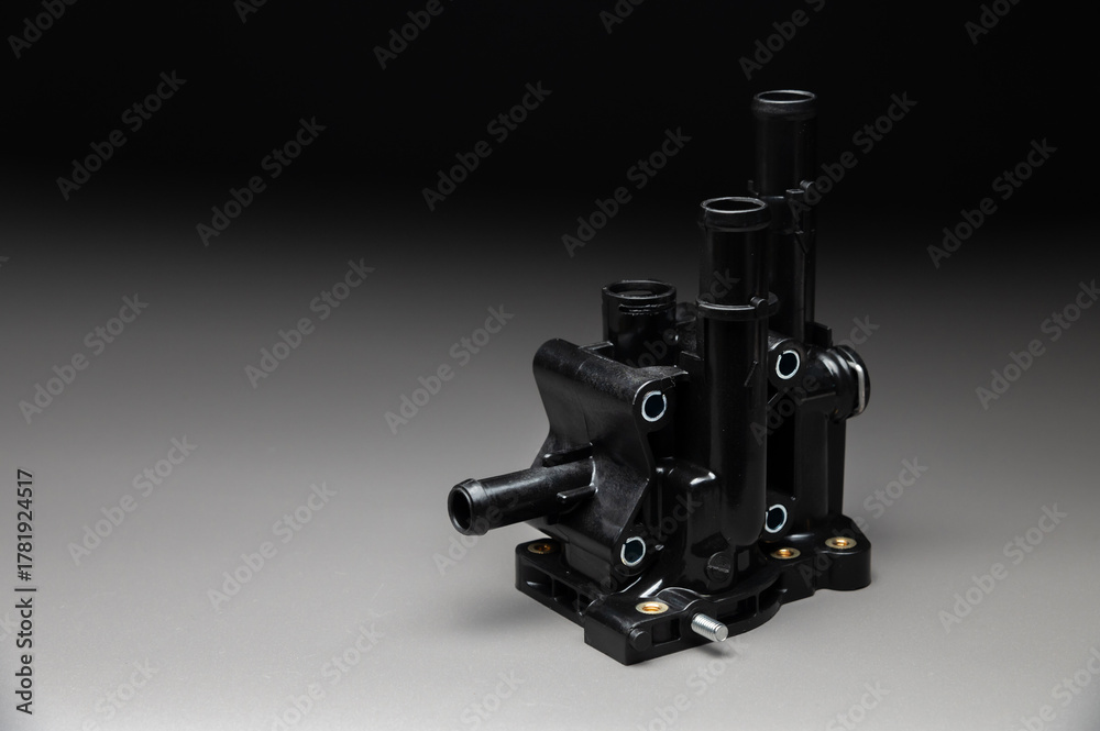 Fototapeta premium Plastic thermostat housing for the internal combustion engine cooling system. This spare part of the car's engine cooling system is on a gray gradient background.