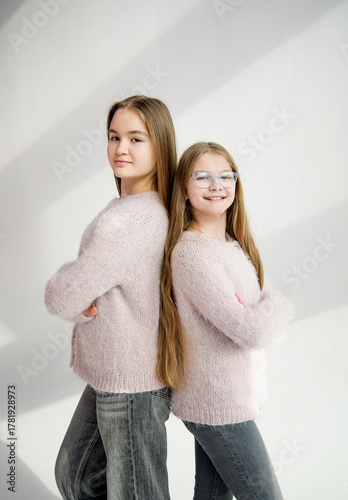 two cute beautiful sisters in pink handmade sweaters hugging in white studio