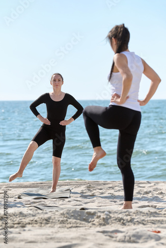 Young female yoga instructor coaching practice on Baltic Sea beach