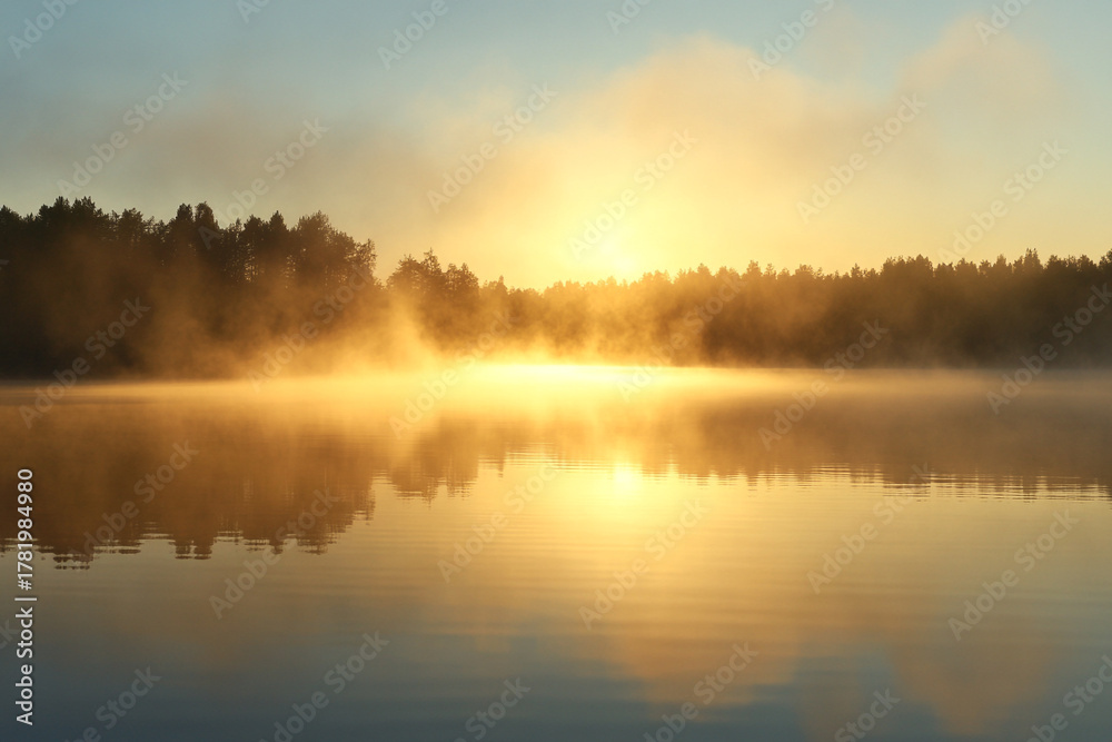 Fototapeta premium foggy lake at sunrise, where the reflection of golden mist hovers over the water