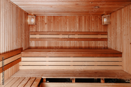 Warm cozy sauna interior with wooden walls, ceiling and floor, featuring a stove with hot stones in the corner. Soft and dim lighting creates a relaxing and intimate atmosphere.