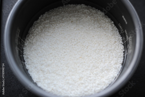 White rice in a rice cooker covered in water ready for boiling as food ingredient