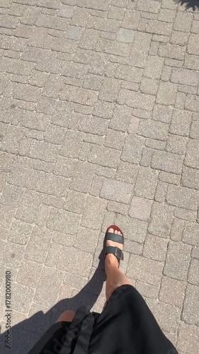personal perspective, woman wearing summer clothes walking alone outdoors on footpath with pavers on a sunny day