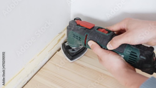 Wallpaper Mural Close-up footage shows skilled hands using electric orbital sander for precise floor edge finishing during interior renovation and restoration work in modern home setting. Torontodigital.ca