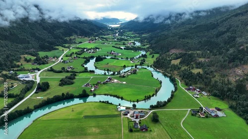 Explore the stunning landscape of Stryn, Norway, featuring vibrant green fields, winding rivers, and picturesque valleys under a dramatic sky. Nature thrives in this serene environment.