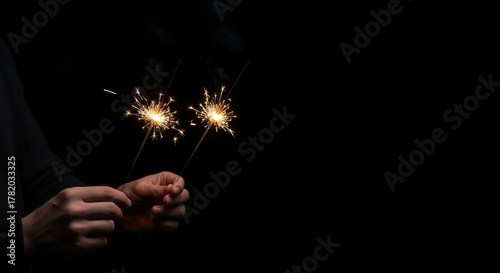 Two Hands Holding Lit Sparklers Against a Pure Black Background with Copy Space