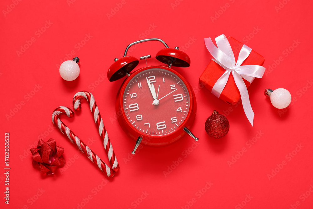 Naklejka premium Alarm clock with Christmas decorations and gift box on red background