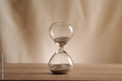 A simple hourglass on a wooden table with a beige backdrop, symbolizing time flow and minimalistic living. Represents timeless themes in a creative, uncluttered presentation for stylish concepts.